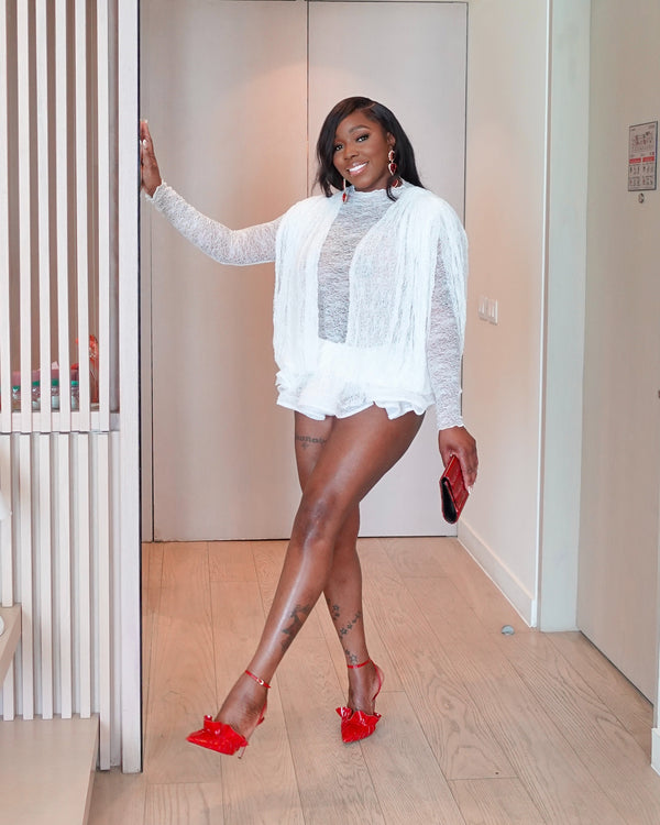 Woman in a white outfit with sheer panels and red high heels standing in a room.